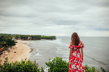 Rare view of brunette woman in red dress enjoy amazing top view of ocean beach from the rockの写真素材