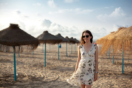 Outdoor portrait of beautiful brunette girl woman on Straw umbrellas background on seaside in sunset light. Sand beach in Valencia.の写真素材