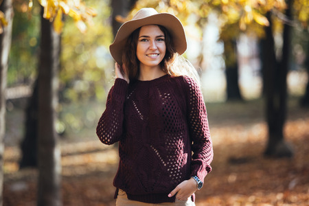 Portrait of happy smile young woman outdoors in autumn park in cozy sweater and hat. Warm sunny weather. Fall concept. Copy space.の写真素材