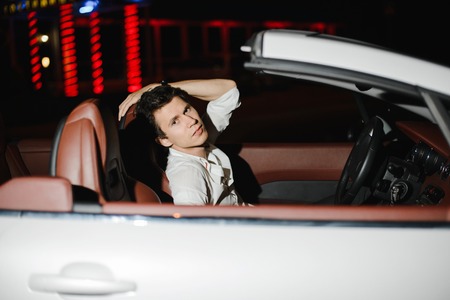 Portrait of a handsome man in white cabriolet. Nightlife. Businessman in suit in luxury carの写真素材