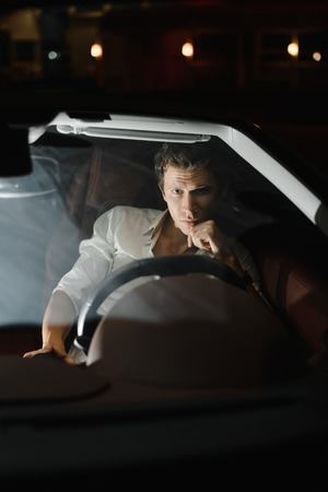 Handsome fashion man driving a car cabriolet. Luxury. Night life.The traffic lights behind him.の写真素材