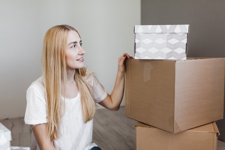 Young woman moving into new apartment holding cardboard boxes with belongings.Photo of young blonde...
