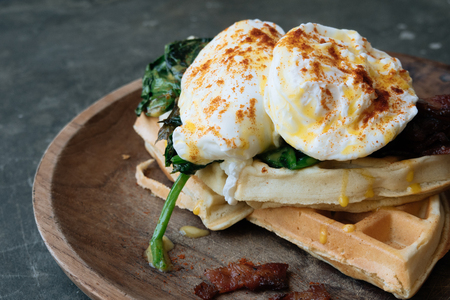 Close up Breakfast with Poached Egg on waffle with spinach and bacon on wooden texture plate on grey stone table. Top viewの写真素材