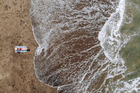 Aerial view of woman sunbath in red bikini and straw hat tanned on towel on ocean beach with black...