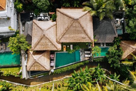 Top drone view of luxury hotel with straw roof villas and pools in tropical jungle and palm trees....