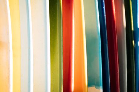 Close up Set of different color surf boards in a stack on sandy beach for rent. Multicolored...