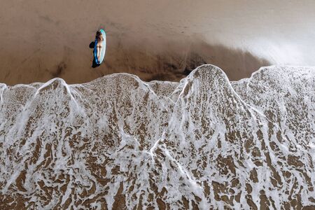 Aerial drone view of a woman on a surfboard on ocean beach of Bali Indonesia. Tropical background...