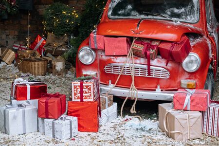 New Year decorated exterior with trunk full of Christmas gifts of retro red car with snow and festive lights and garlands outside of house.の写真素材