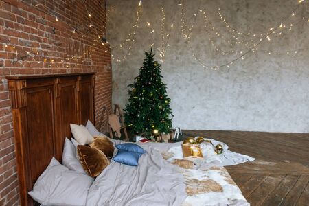 Stylish Christmas interior, bedroom with a lot of lights. Comfort home in a loft style with a decorated Christmas tree and a garland.の写真素材