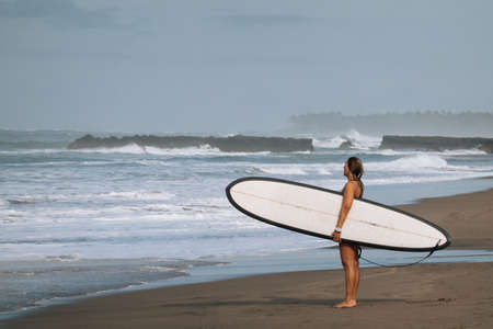 CANGGU, BALI, INDONESIA - FEBRUARY 25, 2019: sporty woman with blue and white surfboard on ocean sand beachのeditorial素材