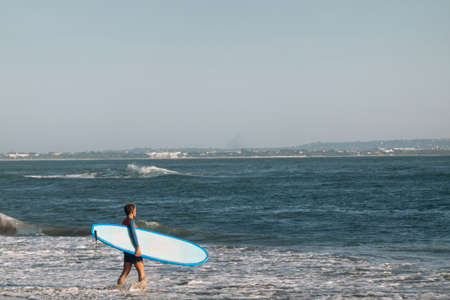 CANGGU, BALI, INDONESIA - FEBRUARY 25, 2019: sporty man with blue surfboard go in water to catch waves in ocean.のeditorial素材