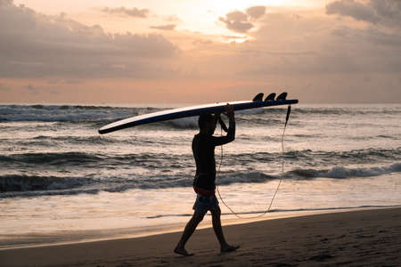 CANGGU, BALI, INDONESIA - FEBRUARY 25, 2019: silhouette of man walking on sea coast with surfboard over head on sunsetのeditorial素材