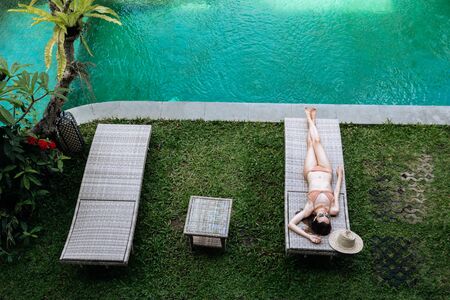 Top view of slim woman in beige bikini take sunbath on lounge chair at the poolside near luxury pool in tropic on vacation.の写真素材