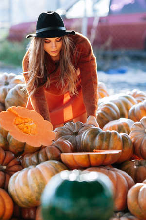 Portrait of happy woman choosing ripe orange pumpkin on farmers market in brown sweater, dress. Cozy autumn vibes Halloween, Thanksgiving dayの写真素材