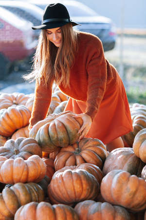 Portrait of happy woman choosing ripe orange pumpkin on farmers market in brown sweater, dress. Cozy autumn vibes Halloween, Thanksgiving dayの写真素材