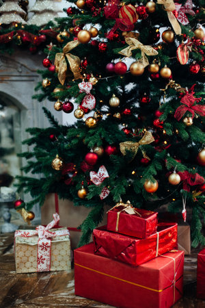 Stacks of Christmas presents in red paper under a Christmas tree decorated red and golden balls near fireplace in living room .New Year interiorの写真素材