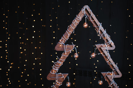 Alternative wooden christmas tree. A handmade New Year tree with light bulb on garland lights black background. Lifestyle trend. Copy space.の写真素材