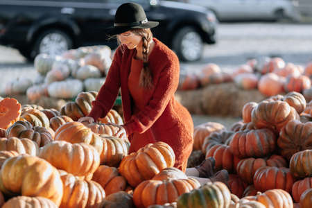 Portrait of happy woman choosing ripe orange pumpkin on farmers market in brown sweater, dress. Cozy autumn vibes Halloween, Thanksgiving dayの写真素材
