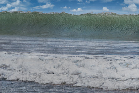 Big wave in the ocean on a sunny day. Blue sky with clouds.