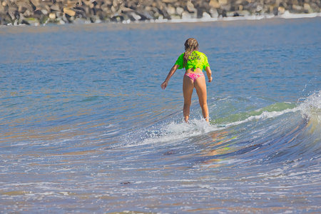 Surfer girl on the beach in a bright sunny day. Rear view.
