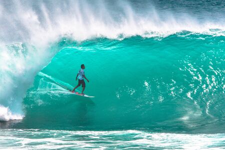 Local surfer riding big green tube section of the wave at Padang Padang beach, Bali, Indonesia