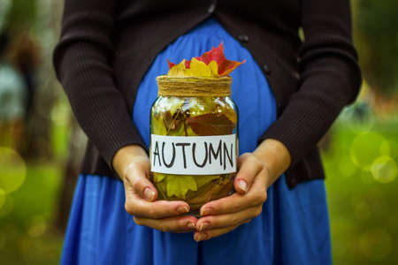 Pregnant girl holding a jar with autumn leaves.の写真素材