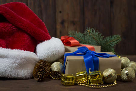 Santa Claus hat, two boxes with gifts with blue and red ribbons, a spruce branch, cones, golden beads, decorative gifts, balls. Focus on a gift with a blue ribbon.の写真素材