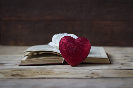 Heart, open book and top of a white rose bud on a wooden background.の写真素材