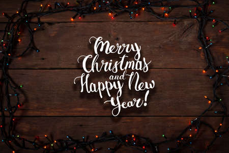 Multicolored garlands on a wooden background. The inscription is added Merry Christmas and Happy New...