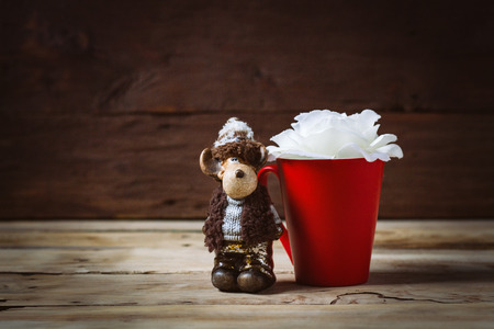 White rose flower in a red cup and toy on a wooden background.の写真素材