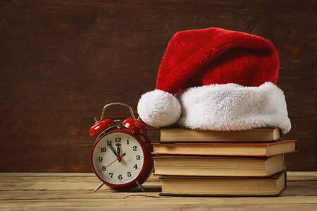 Red alarm clock. On the books Santa's hat, on a wooden background.の写真素材