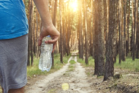 Man holding a bottle of water on the background of a dirt road in the woods. Concept of training in...