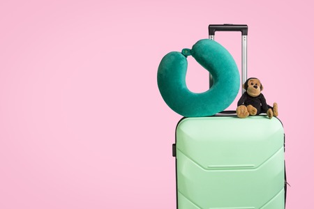 Plastic suitcase with wheels, soft toy, travel pillow, pink background. Travel concept for children, visit to relatives, trip to camp.の写真素材