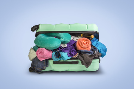 Plastic suitcase with wheels, overflowing things on a blue background. Travel concept, vacation trip, visit to relatives.の写真素材