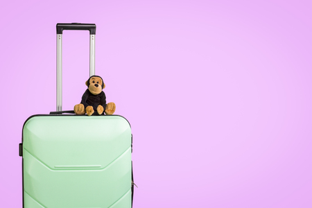 Plastic suitcase with wheels and a soft toy on it, pink background. Travel concept for children, visit to relatives, trip to camp.の写真素材