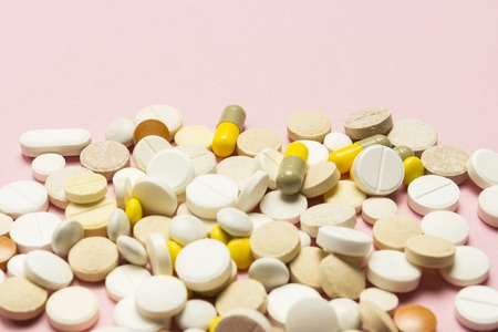 Pills of different sizes and colors on a light pink background. Concept of the pharmaceutical industry, daily vitamins and minerals for women. Pregnancy, menopause.の写真素材