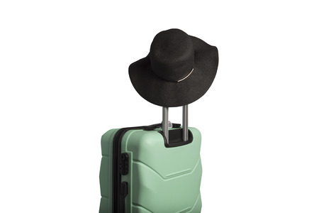 Plastic suitcase on wheels and a hat with a wide brim on the handle on a white background. Isolated. Travel concept, vacation trip, visit to relatives.の写真素材
