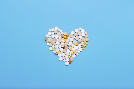 Pills of different colors and sizes on a blue background. Heart shape. Concept of the pharmaceutical industry, medicine, treatment and recovery after illness. Flat lay, top view.の写真素材