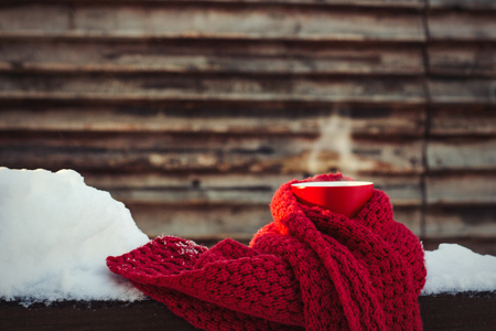 Red Cup with Hot Tea and Red Scarf on the Snowy Wooden Background. Winter Concept. Sunny day. Winter holidays.の写真素材