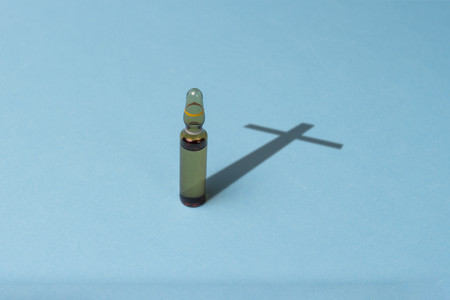 Vaccine ampoules and a shadow in the form of crosses on a blue background. The concept of vaccination death, drug addiction, dependence on medical priporatov, low-quality drugs.の写真素材
