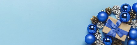 Gift box with blue ribbon, Christmas-tree decorations, balls and white and gold pine cones on a blue background. Concept of Merry Christmas and Happy New Year. Minimalism. Flat lay, top view. Banner.の写真素材