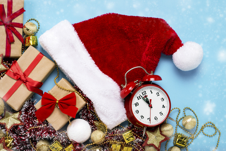 Red alarm clock, Santa Claus hat, Christmas-tree decorations, gifts on a blue background. Merry Christmas and happy new year concept. Flat lay, top view.の写真素材