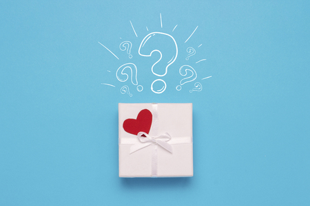 White gift box, red heart and Icon Question mark on a blue background. Minimalistic style. Concept surprise and suspense, a gift from a loved one. Flat lay, top view.の写真素材