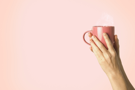Female hand holding a purple cup with hot coffee or tea on a light pink background. Breakfast concept with hot coffee or tea.の写真素材