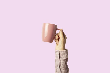 Female hand holding a purple cup with hot coffee or tea on a light pink background. Breakfast concept with hot coffee or tea.の写真素材