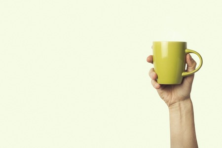 Female hand holding a green cup with hot coffee or tea on a light green background. Breakfast concept with hot coffee or tea.の写真素材