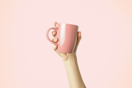 Female hand holding a purple cup with hot coffee or tea on a light pink background. Breakfast concept with hot coffee or tea.の写真素材