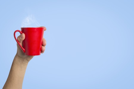Male hand holding a red cup with hot coffee or tea on a light blue background. Breakfast concept with hot coffee or tea.の写真素材