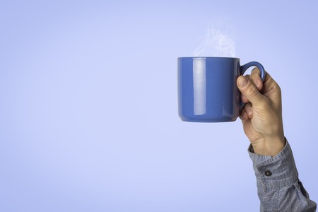 Male hand holding a blue cup with hot coffee or tea on a light blue background. Breakfast concept with hot coffee or tea.の写真素材