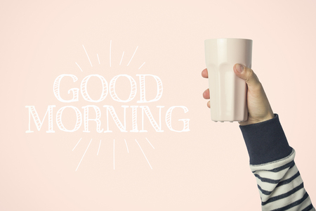 Male hand holding a purple cup with hot coffee or tea on a pink background. Added text Good morning. Breakfast concept with hot coffee or tea.の写真素材